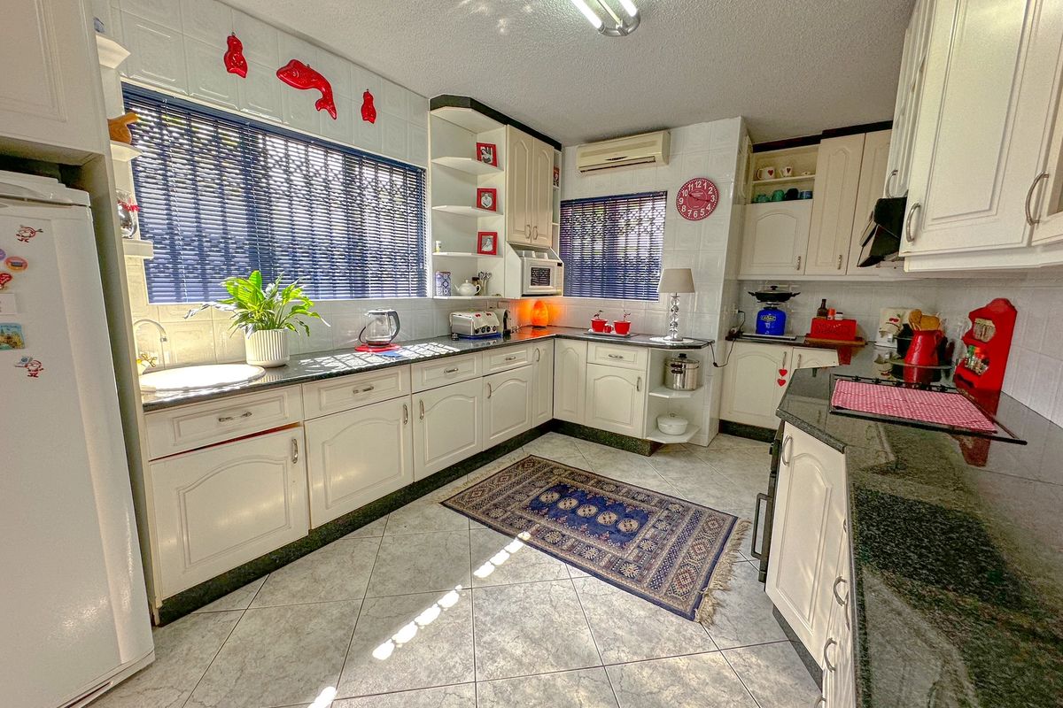 A functional kitchen featuring white cabinetry, dark granite countertops, tiled flooring, and integrated wall-mounted air conditioning unit.