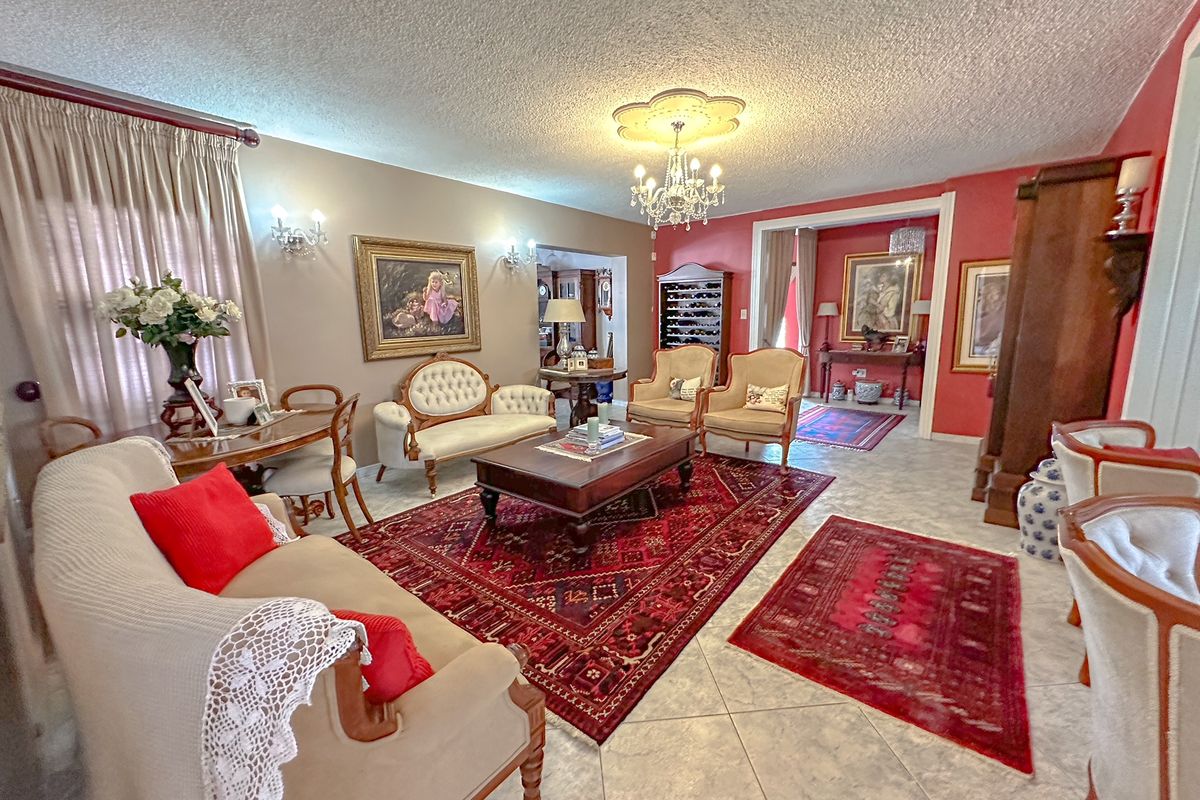Spacious living area featuring a decorative ceiling rose, crystal chandelier, and tiled flooring, providing a formal and traditional atmosphere.