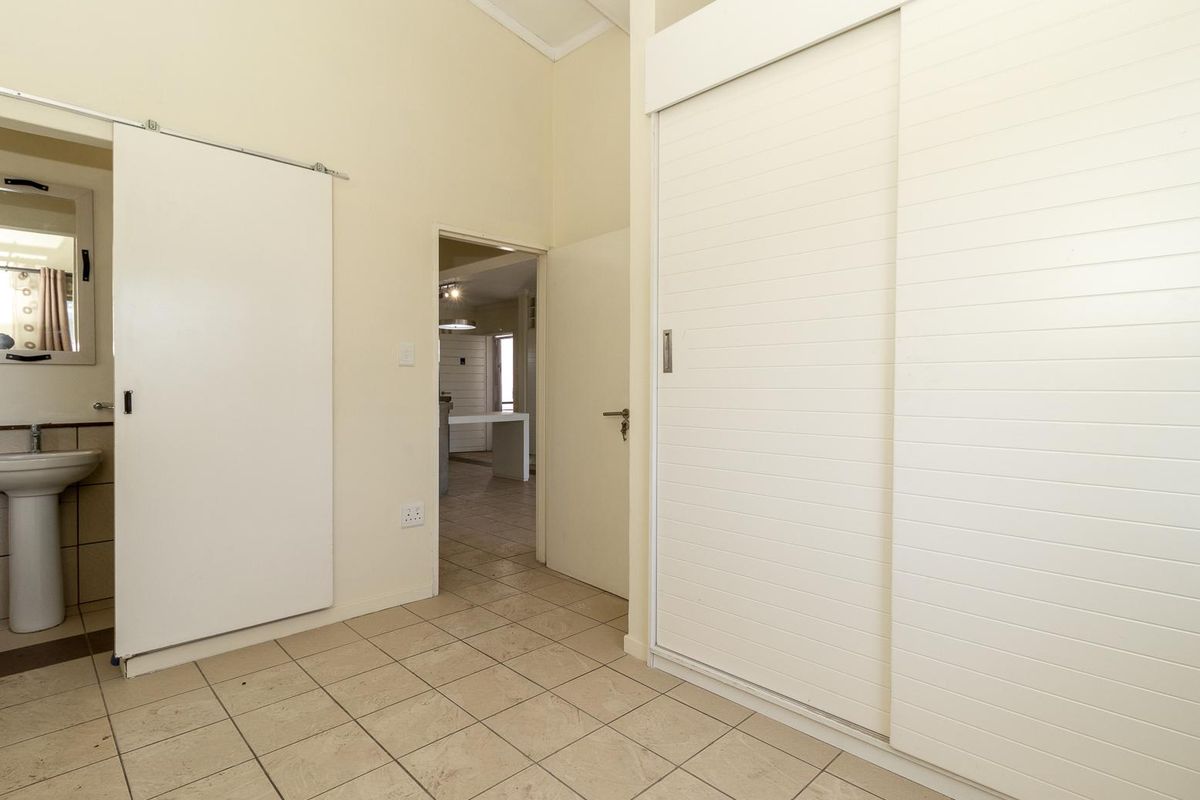 A spacious bedroom featuring built-in sliding door wardrobes, tiled flooring, and an en-suite pedestal basin area, offering a clean and functional layout.