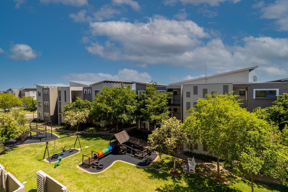 Elevated view of the apartment complex grounds featuring a well-maintained garden, mature trees, and a dedicated children's play area.