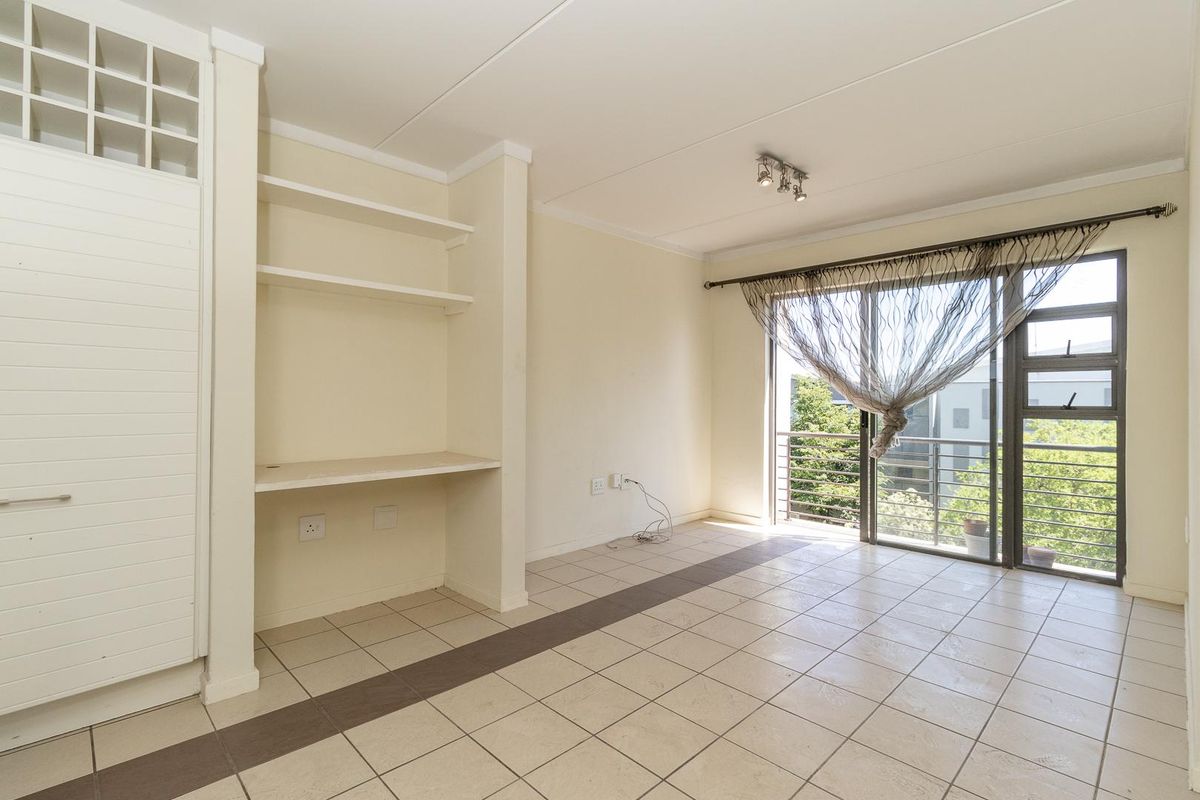 An empty living area featuring tiled floors, built-in shelving with a desk, and a sliding glass door leading to a balcony.