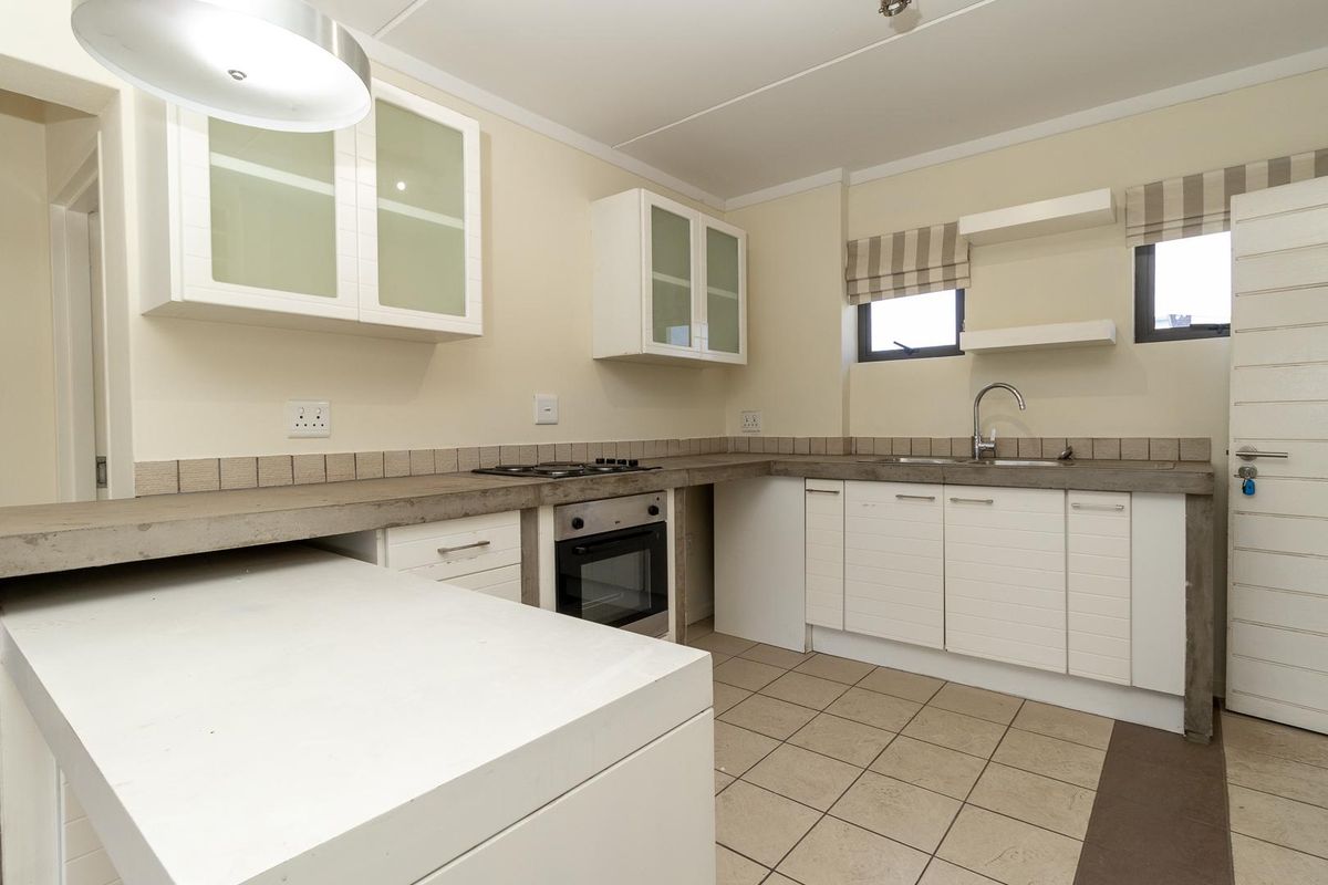 A clean, functional kitchen featuring white cabinetry, concrete countertops, built-in oven, gas hob, and tiled flooring with ample storage space.