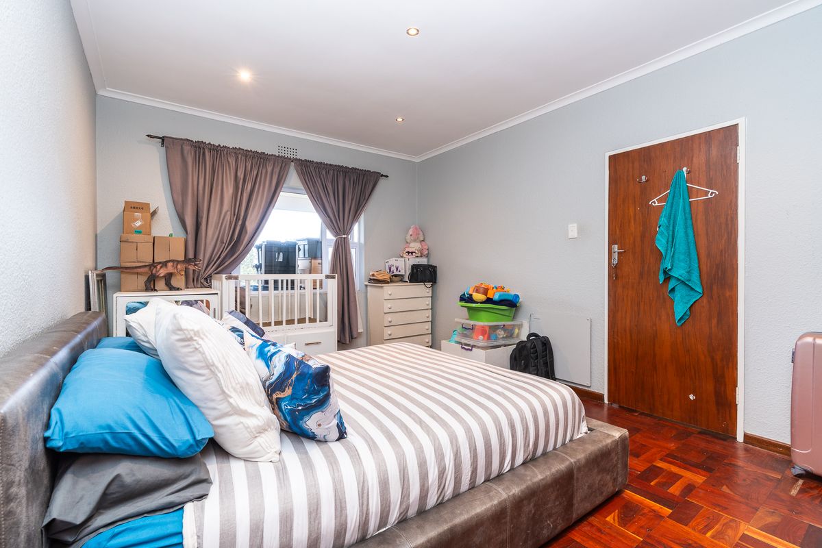 A bedroom featuring warm parquet flooring, recessed downlighting, and a solid timber door, offering a functional space with neutral wall finishes.