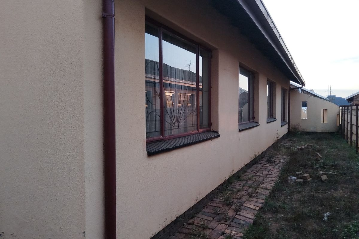 Side view of the property exterior featuring a brick pathway, metal window frames with security bars, and a downpipe along the wall.