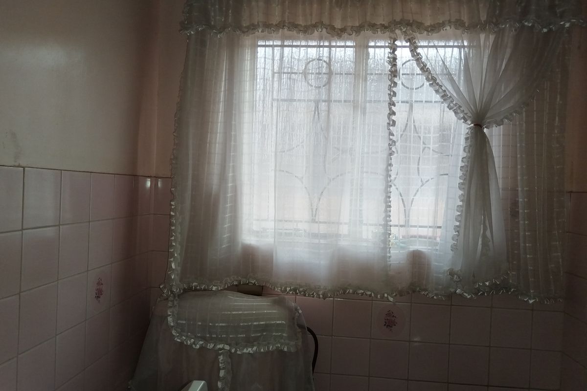 A bathroom space featuring dated pink ceramic wall tiles and a window fitted with security bars.
