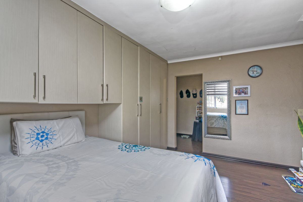 Bedroom featuring extensive built-in cupboard storage, laminate flooring, and neutral wall tones, offering a functional layout with direct access to an adjacent space.