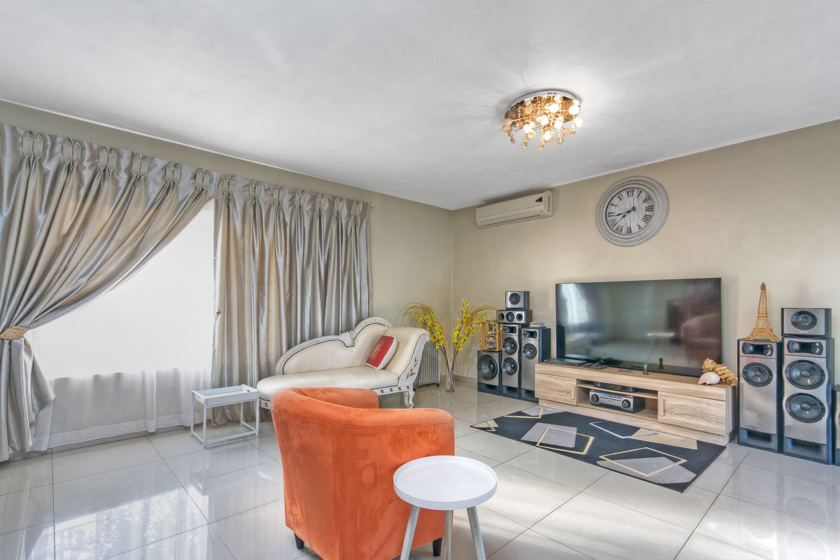 A well-maintained living room featuring polished tiled flooring, a wall-mounted air conditioning unit, and decorative ceiling lighting.