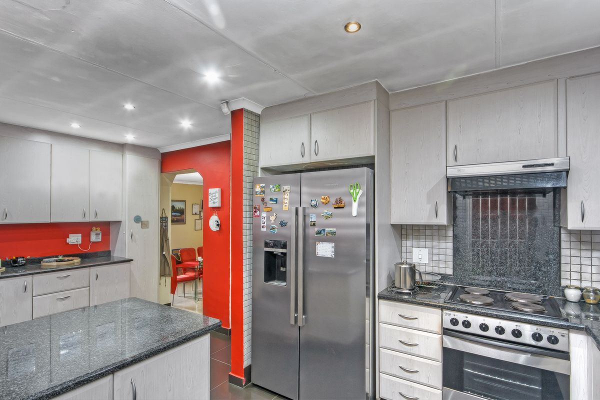 A functional kitchen featuring granite countertops, built-in cabinetry, an integrated oven with hob, and a tiled backsplash, leading into an adjacent dining area.