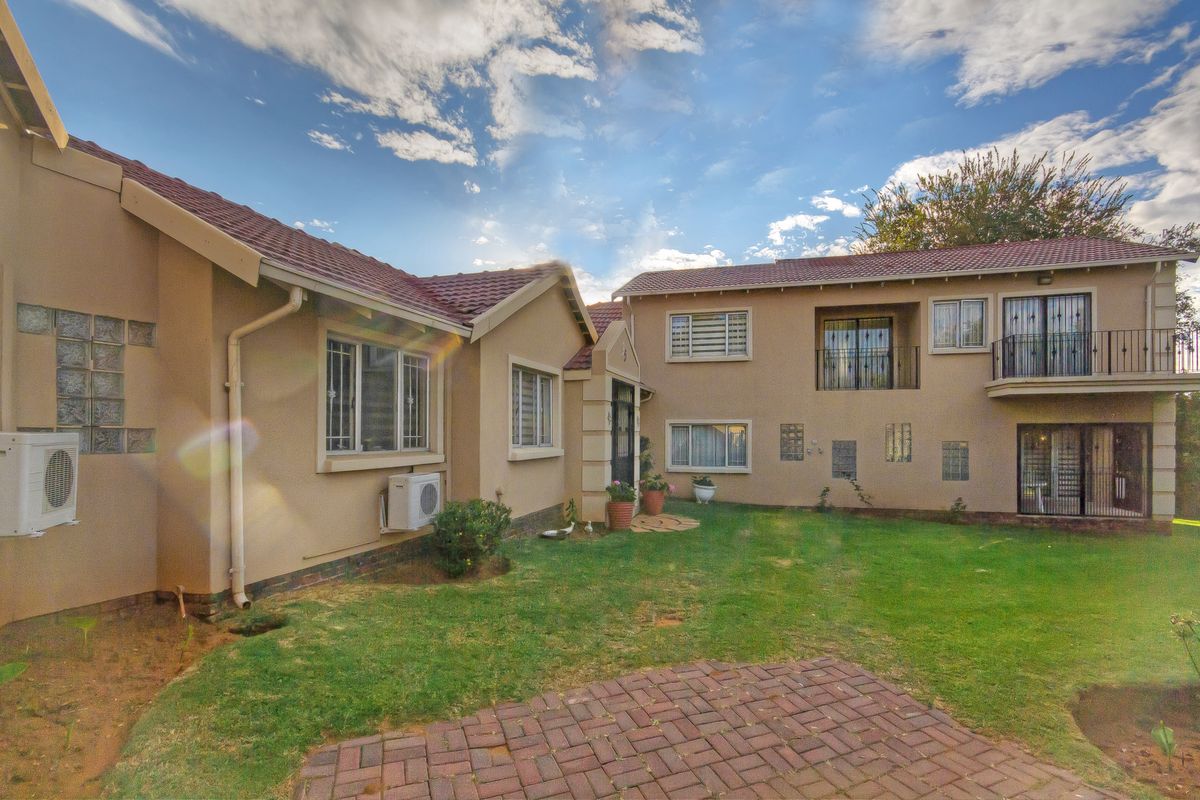 Rear view of a multi-level residential property featuring a tiled roof, brick paved area, lawn, and security-fitted windows and balcony.