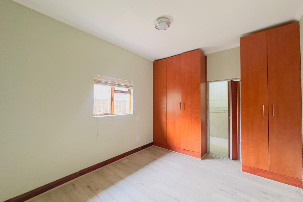 A bright, empty bedroom featuring laminate flooring, built-in wooden cupboards, and direct access to an en-suite bathroom.