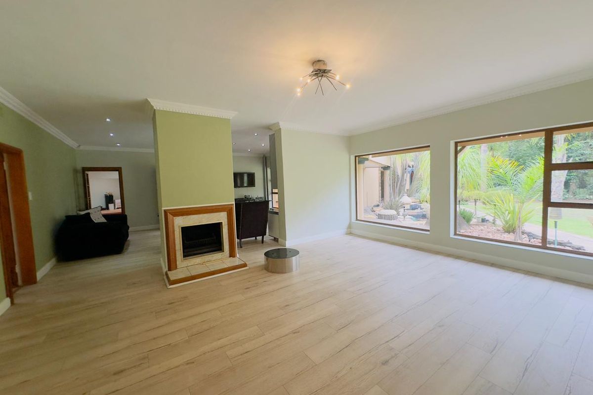 Spacious living room featuring light wood-look laminate flooring, a central fireplace, and large windows providing natural light and garden views.
