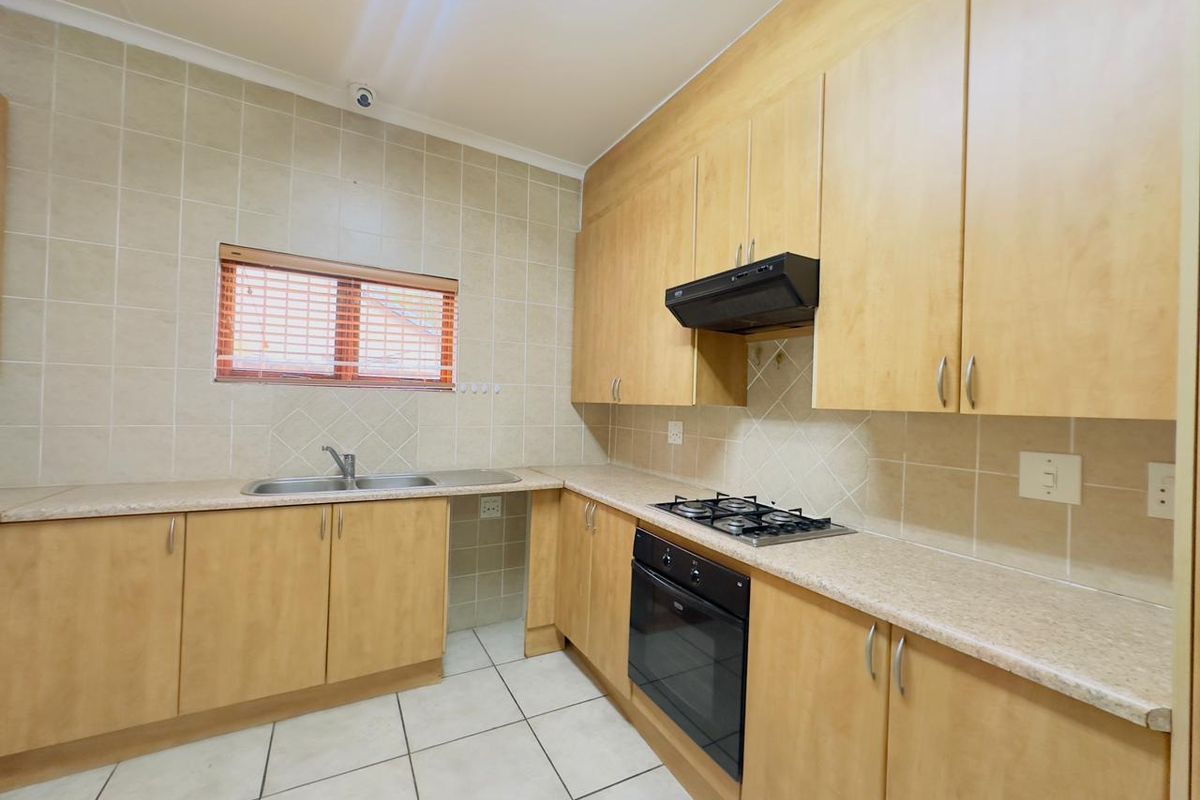 A functional kitchen featuring light wood-finish cabinetry, laminate countertops, a built-in oven with gas hob, and neutral ceramic tiling throughout.