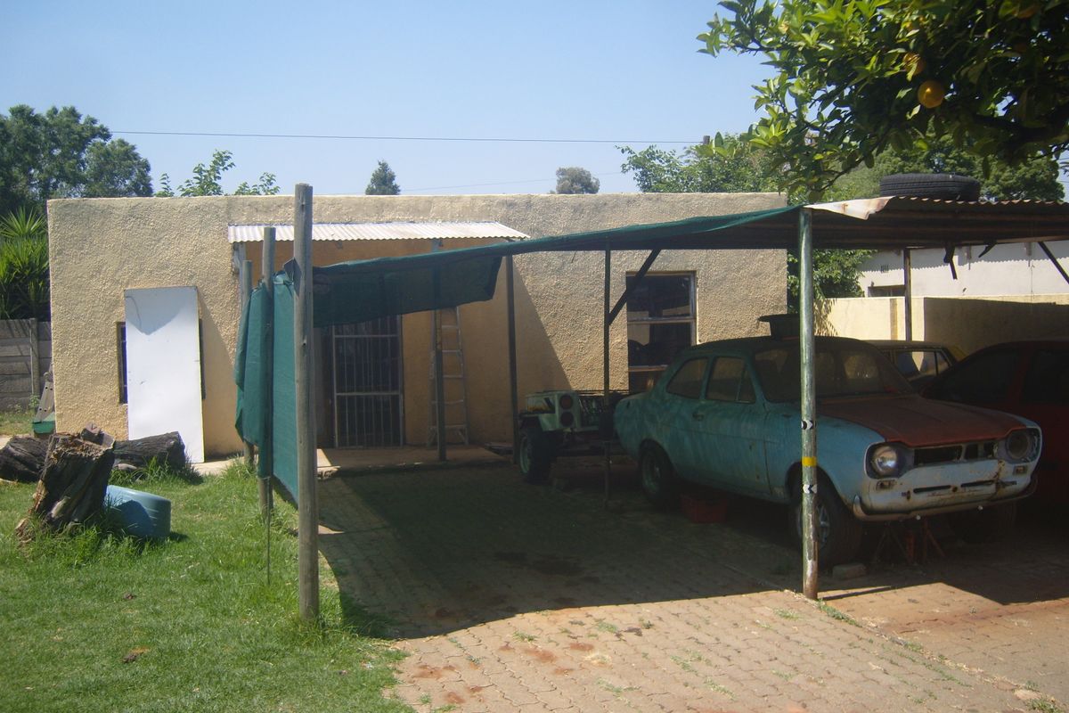 Rear exterior view of the property featuring a basic carport structure, paved driveway, and a stucco-finished building facade with security gate.