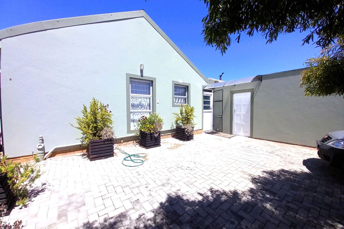 A paved rear courtyard area featuring a light-colored exterior wall, secure door access, and a small covered entryway.