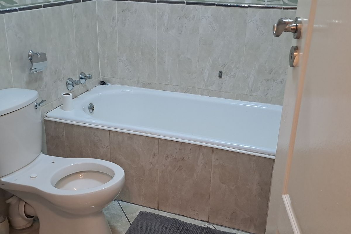 A functional bathroom featuring a bathtub with tiled surround, a standard toilet, and a wall-mounted basin with tiled walls.