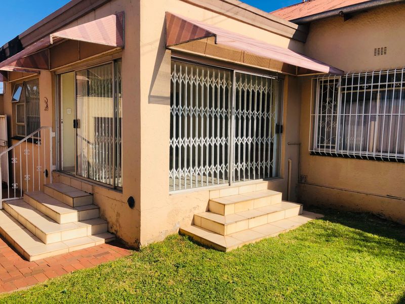 Rear exterior view of the house featuring tiled steps, sliding glass doors with security gates, and metal awnings over the entrance.