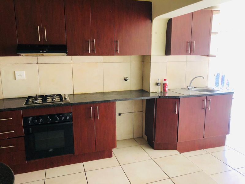 A functional kitchen featuring dark wood cabinetry, granite countertops, a built-in gas hob, oven, and a stainless steel sink with tiled backsplash.