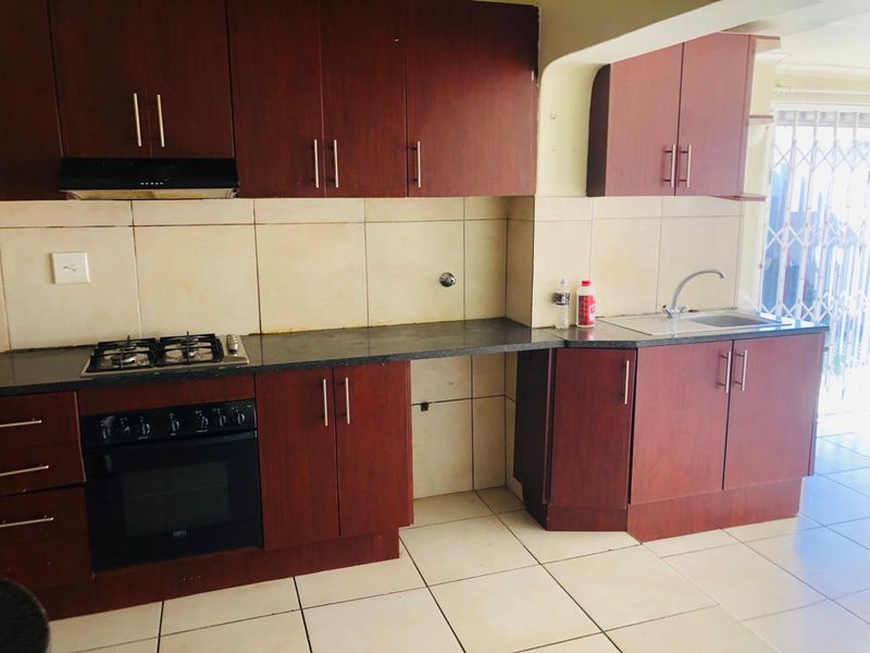 A functional kitchen featuring dark wood cabinetry, granite countertops, a gas hob, built-in oven, and tiled finishes throughout.