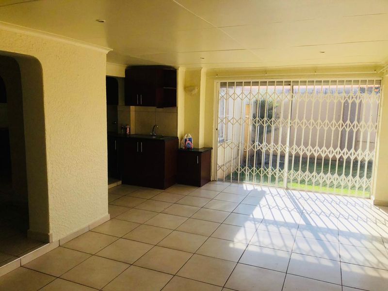 Open plan living area featuring tiled flooring, built-in kitchen cabinetry, and a sliding glass door with security gate leading to the rear garden.