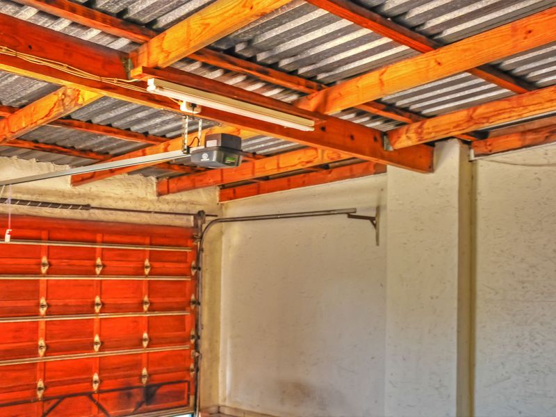 A functional garage space featuring exposed timber roof trusses, corrugated metal roofing, and an automated sectional garage door mechanism.