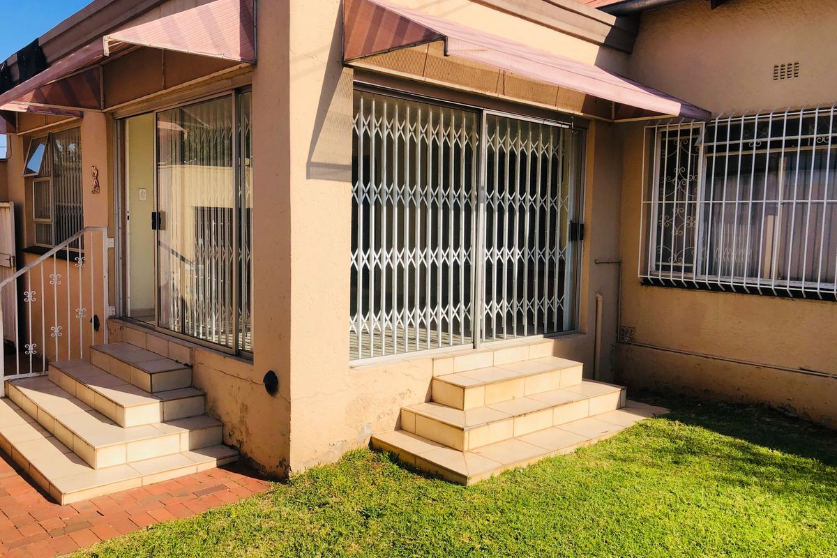 Rear exterior view of the house featuring tiled steps, sliding glass doors with security gates, and metal awnings over the entrance.