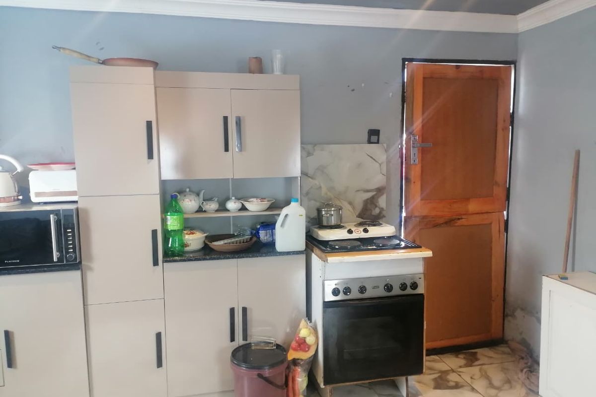 A compact kitchen featuring built-in cabinetry, a freestanding stove with oven, and tiled flooring, with direct access to an exterior timber door.