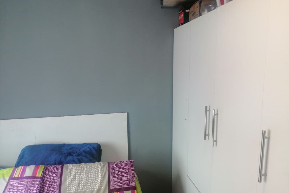 A bedroom featuring a built-in white wardrobe with modern handles and a grey accent wall.