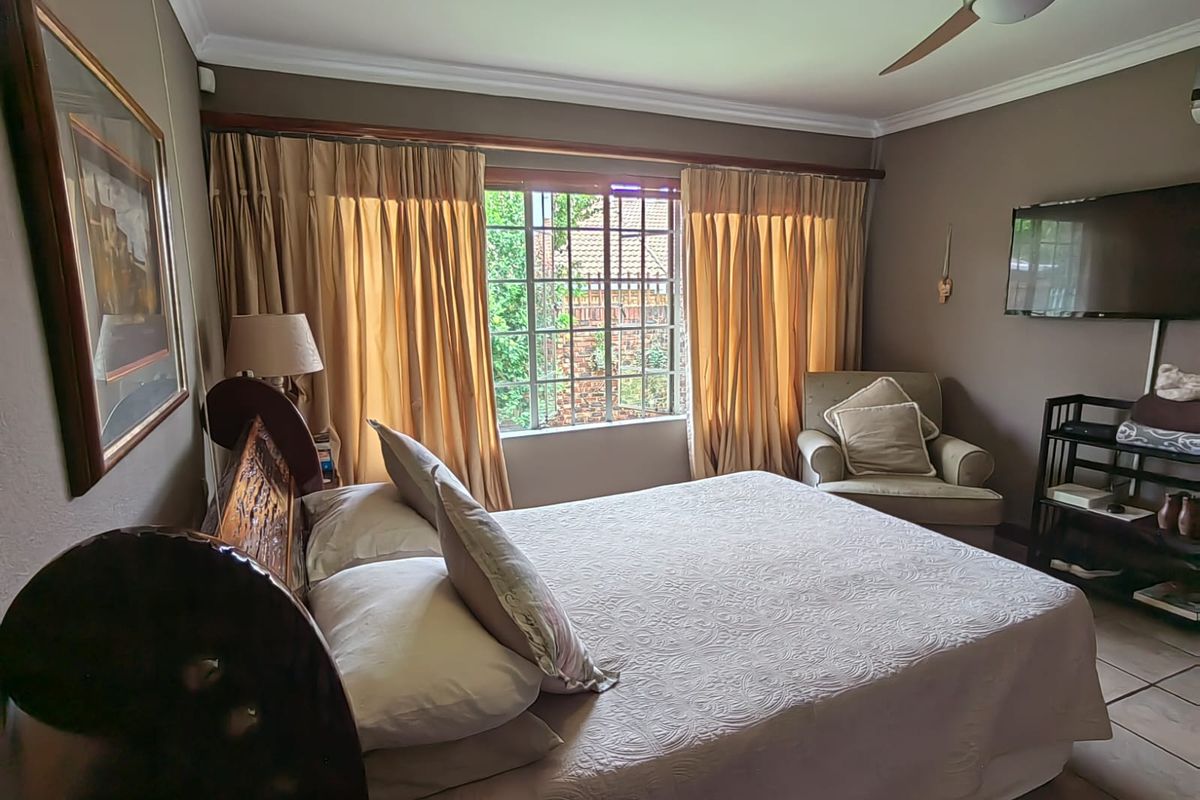 A comfortable bedroom featuring tiled flooring, a ceiling fan, and a window with security bars, providing a functional and well-maintained living space.