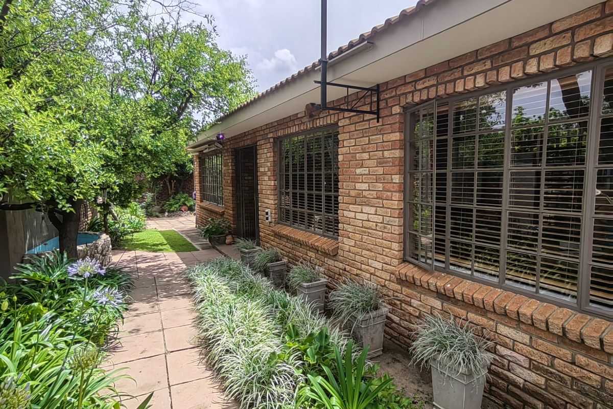 A well-maintained rear exterior view of the house featuring face brick walls, a tiled roof, and a landscaped garden with a paved walkway.