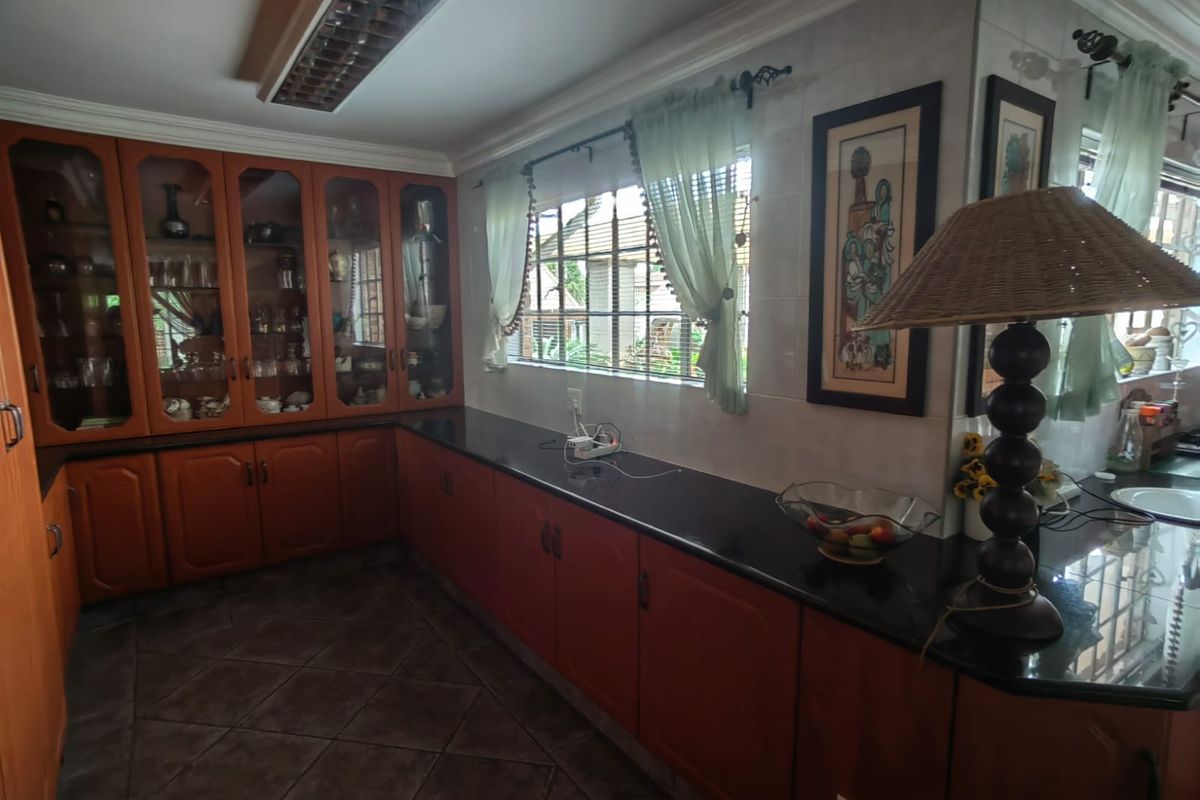 A kitchen area featuring extensive wooden cabinetry, dark granite countertops, and tiled flooring, offering ample storage and workspace.