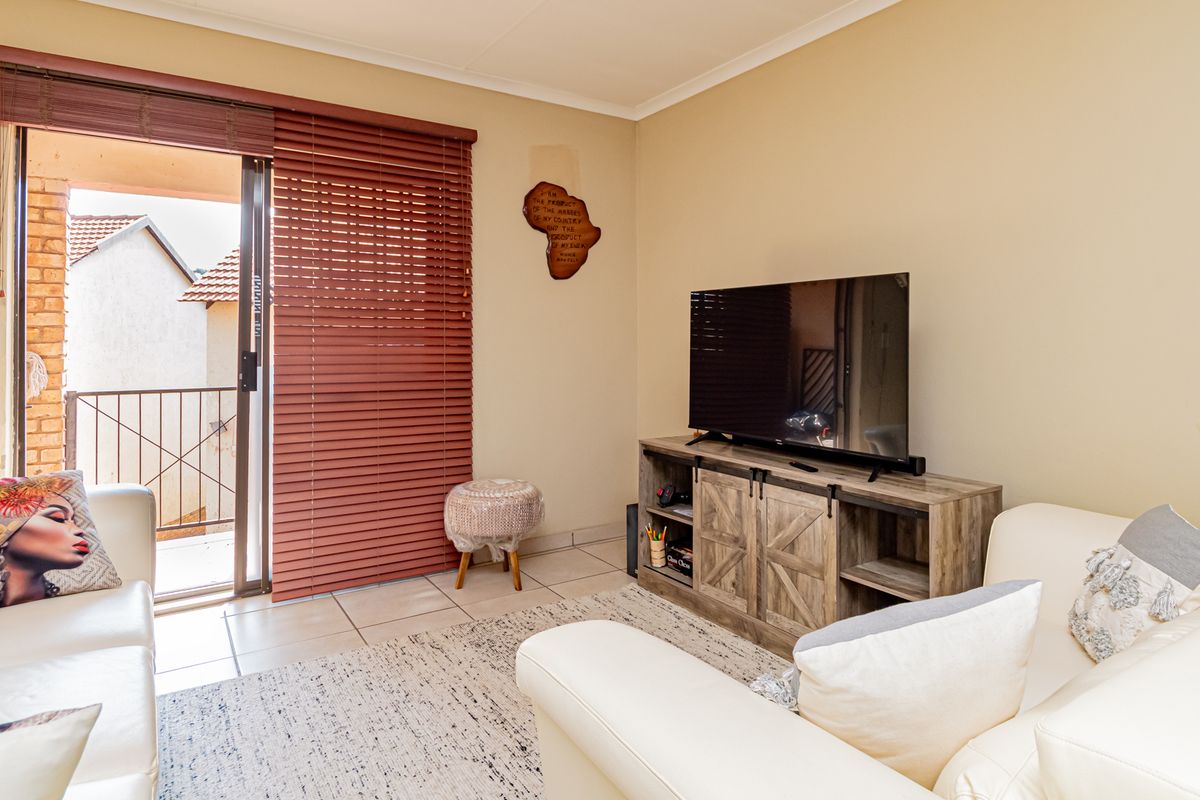 A living room featuring tiled flooring and a sliding glass door leading to a balcony, with visible wall surface imperfections requiring attention.