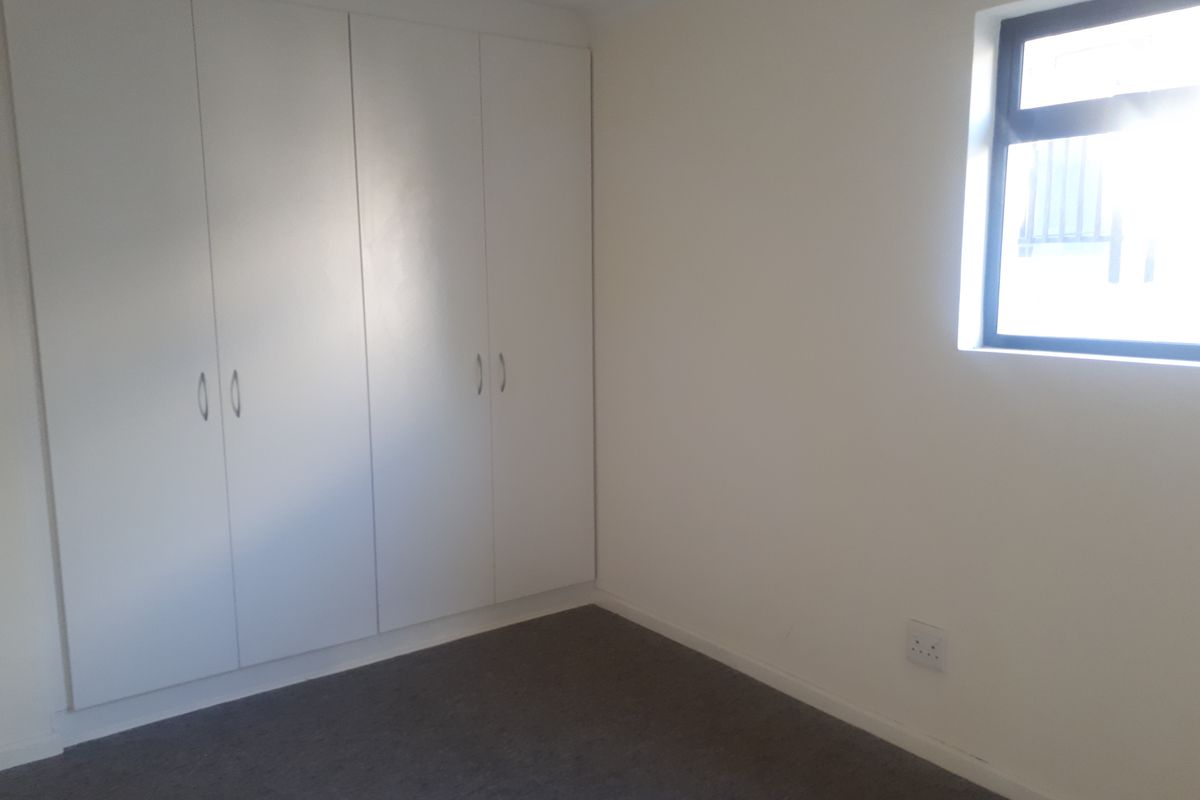 A clean, empty bedroom featuring neutral walls, carpeted flooring, and built-in cupboards, providing a versatile space ready for personalization.