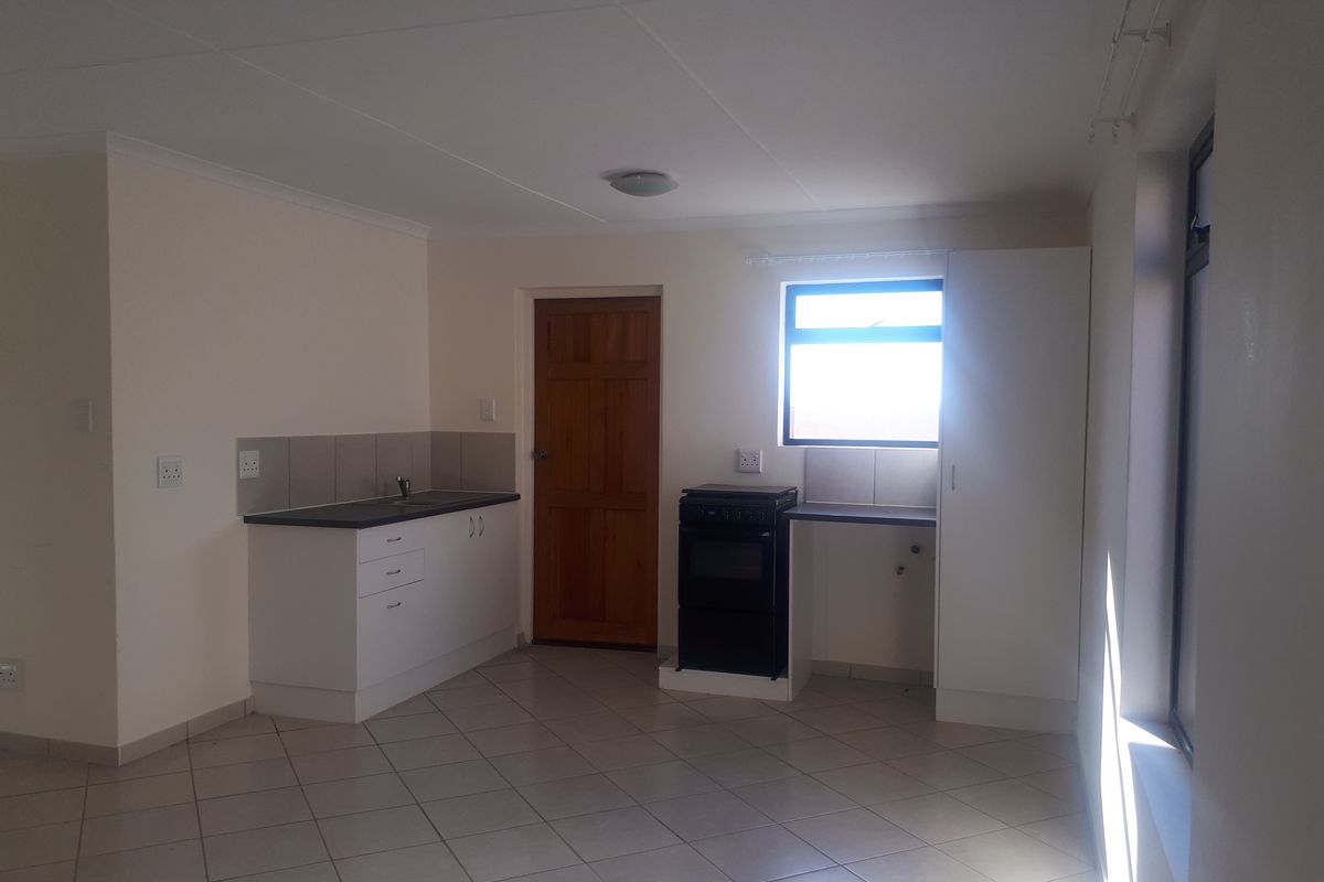 A functional, empty kitchen featuring white cabinetry, dark laminate countertops, tiled flooring, and a freestanding stove, offering a clean canvas for potential updates.