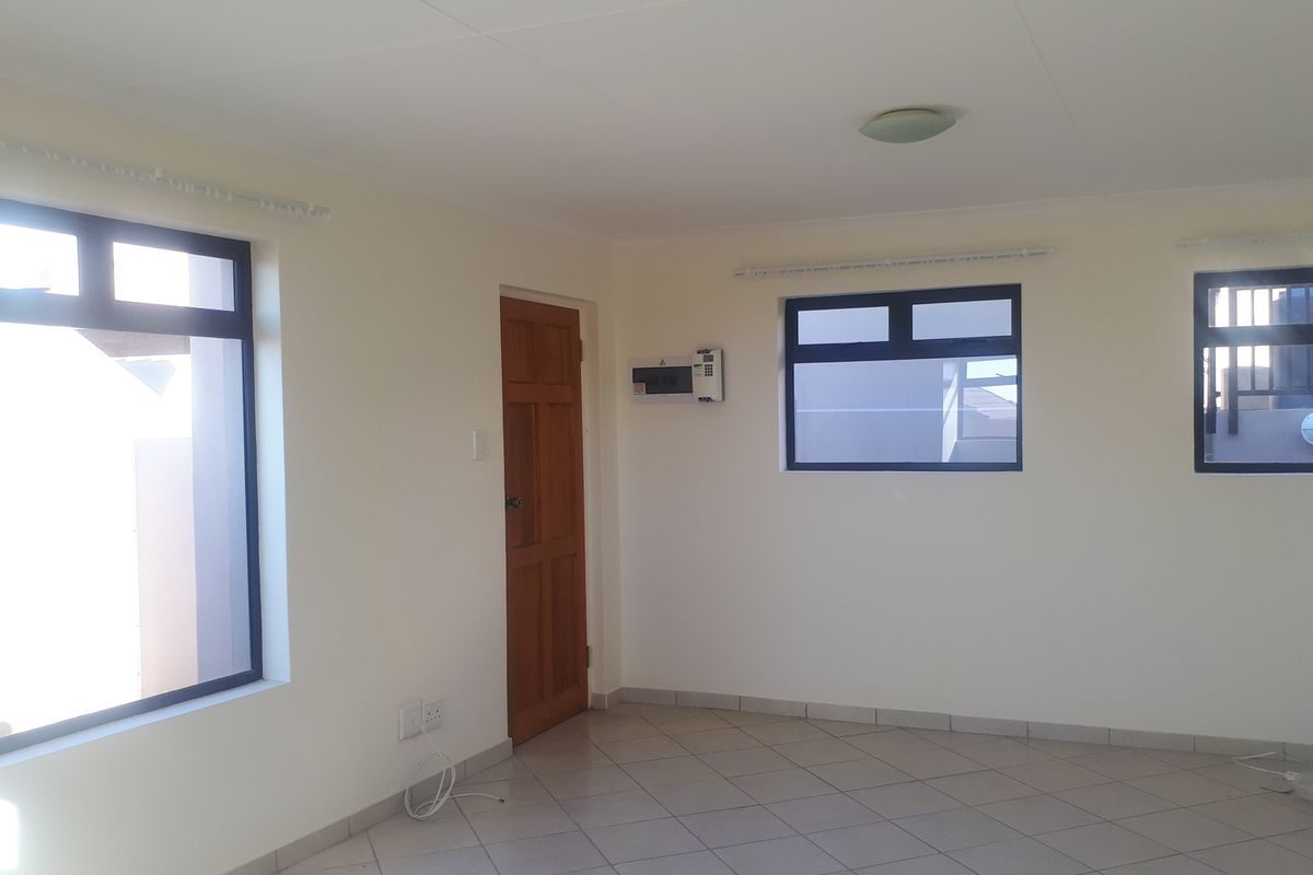 A bright, empty living area featuring neutral tiled flooring, clean white walls, and aluminium-framed windows, providing a versatile blank canvas for interior design.