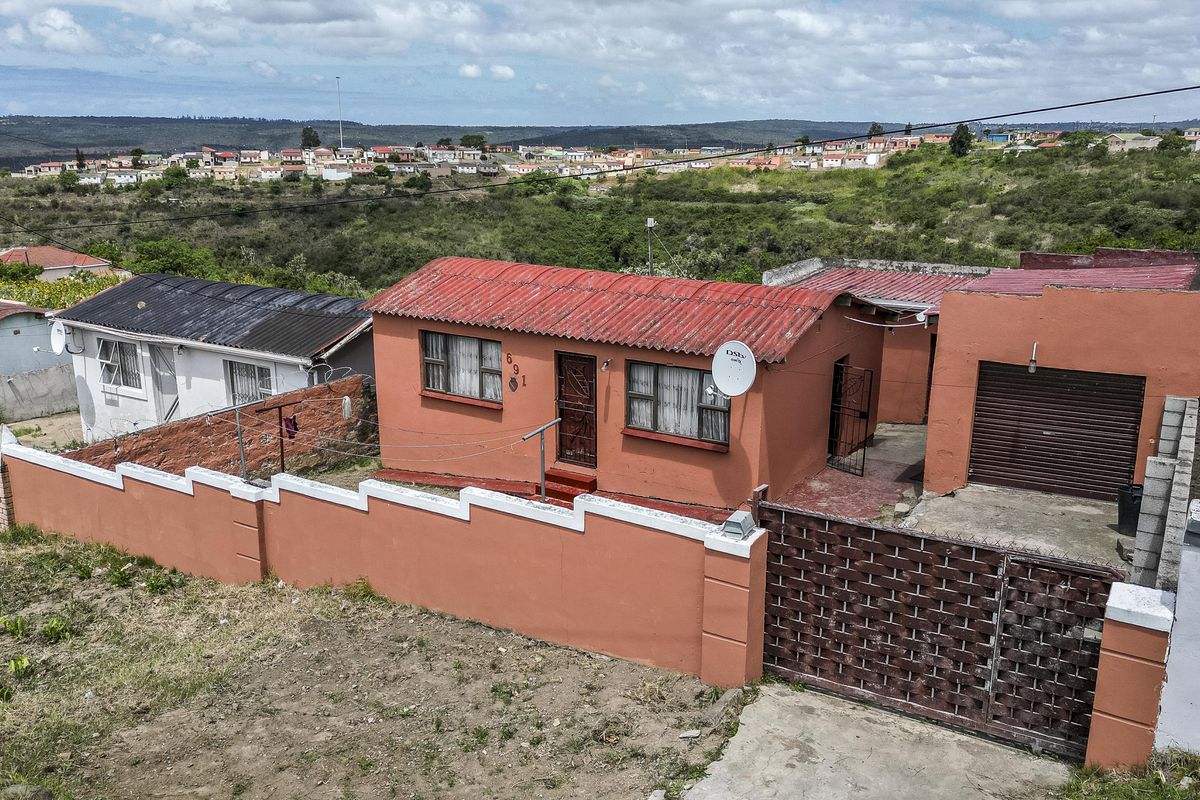 Aerial view of a residential property featuring a corrugated metal roof, perimeter wall, and attached garage in a suburban setting.