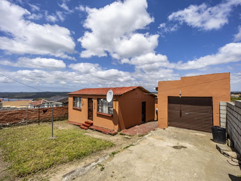 Rear view of the property featuring a small house, a detached garage with a roller door, a concrete driveway, and a fenced garden area.