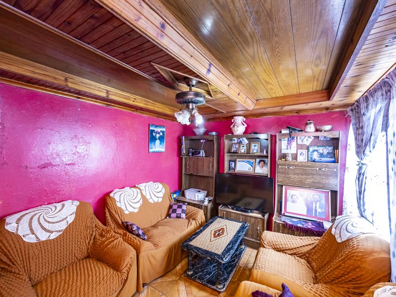 A living room featuring a distinctive timber-clad ceiling, parquet flooring, and a ceiling fan, requiring cosmetic updates to the wall finishes.