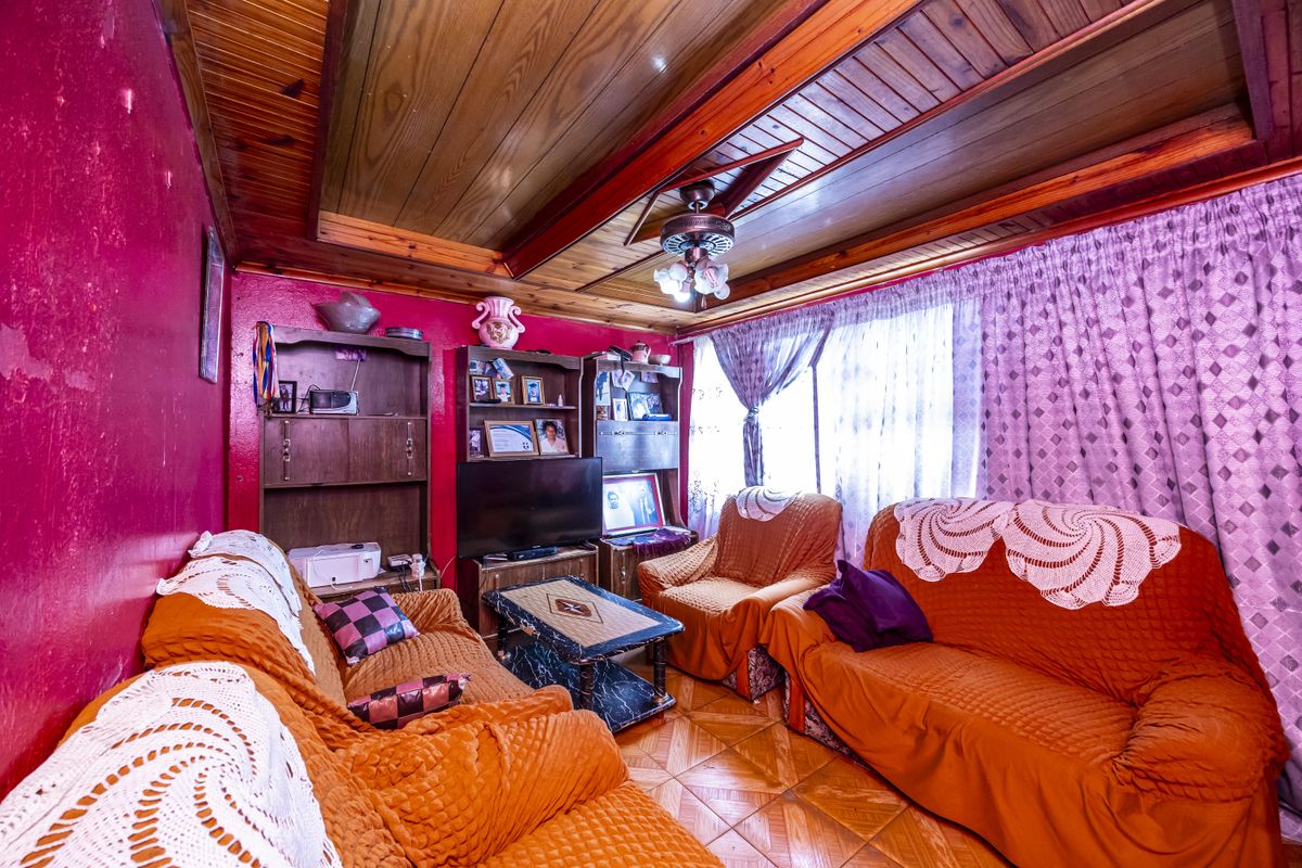 A living room featuring a timber-clad ceiling, ceiling fan, and tiled flooring, currently requiring cosmetic updates to the wall finishes.