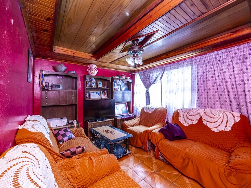 A living room featuring a timber-clad ceiling, ceiling fan, and tiled flooring, currently requiring cosmetic updates to the wall finishes.
