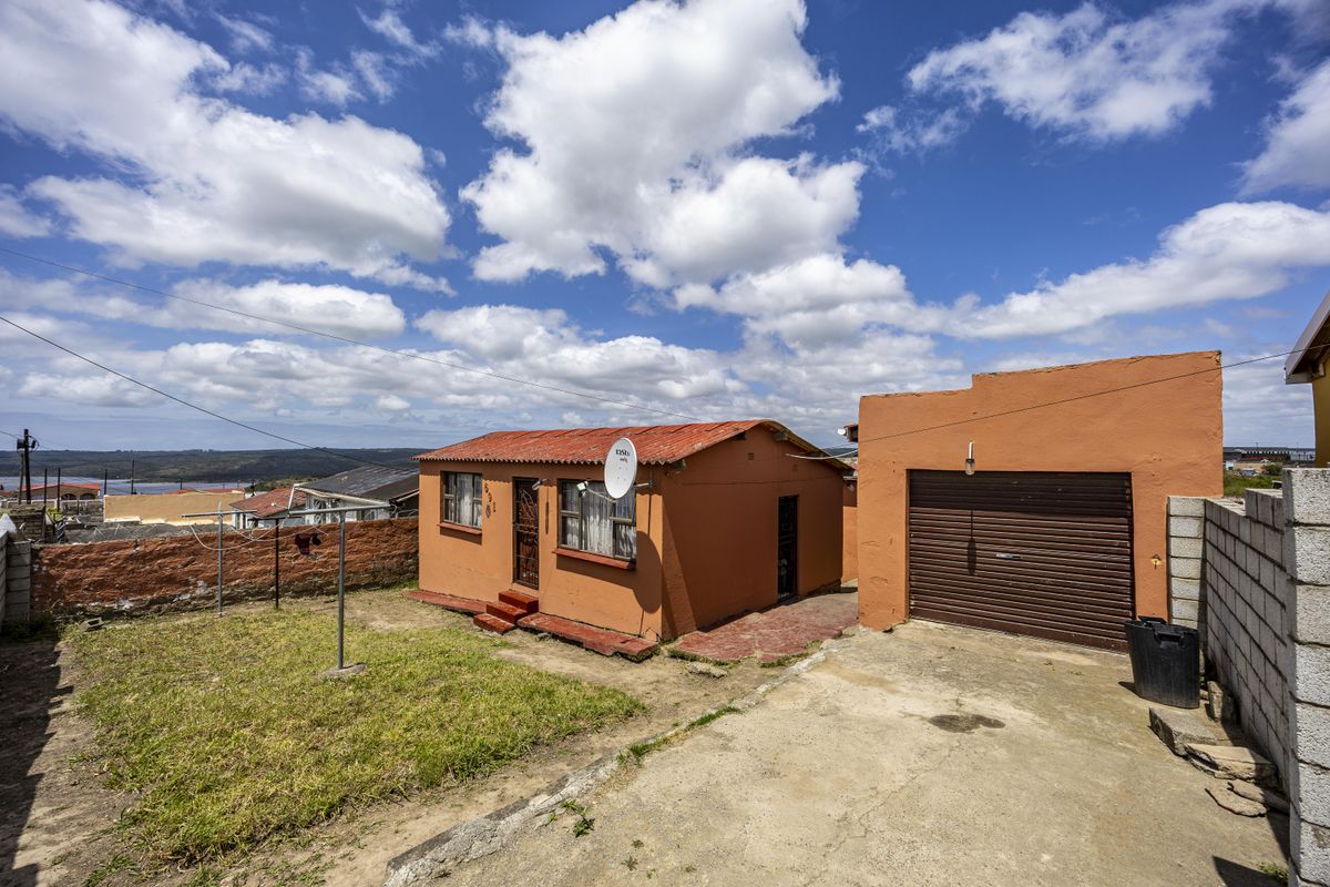 Rear view of the property featuring a detached single garage, concrete driveway, and a small yard area with boundary walling.