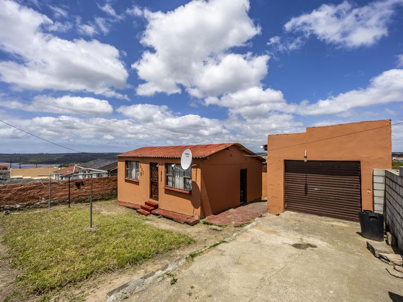 Rear view of the property featuring a detached single garage, concrete driveway, and a small yard area with boundary walling.