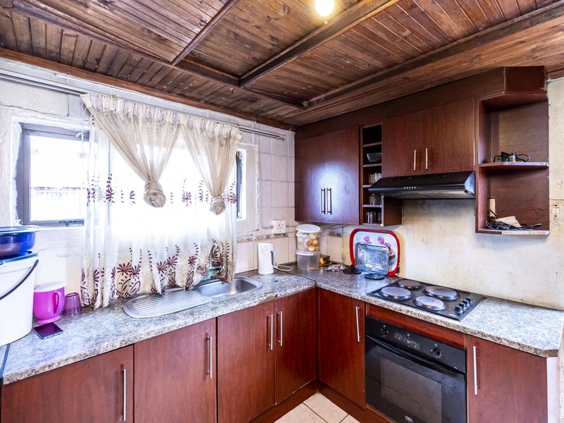 A dated kitchen featuring timber panelled ceilings, built-in wooden cabinetry, laminate countertops, and integrated cooking appliances.