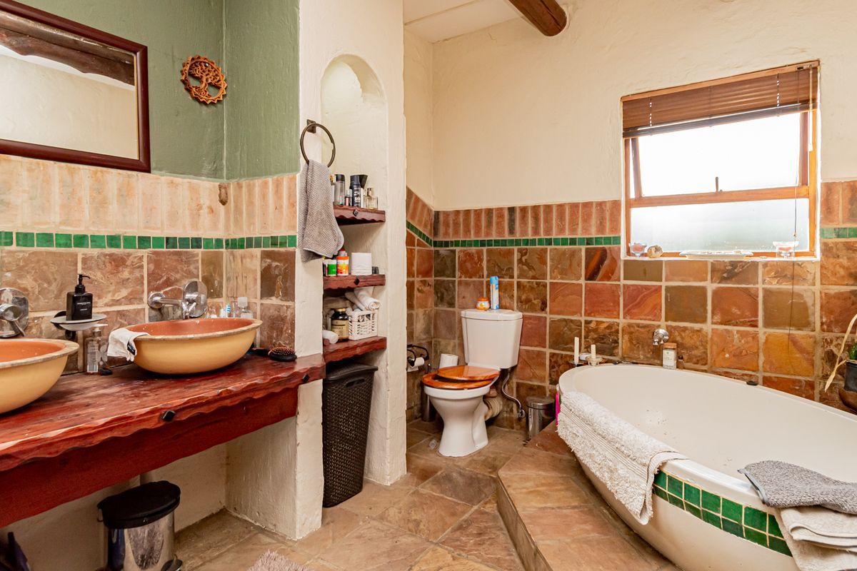 A rustic-style bathroom featuring dual vessel sinks on a wooden vanity, a freestanding bathtub, and earthy stone-tiled walls and flooring.