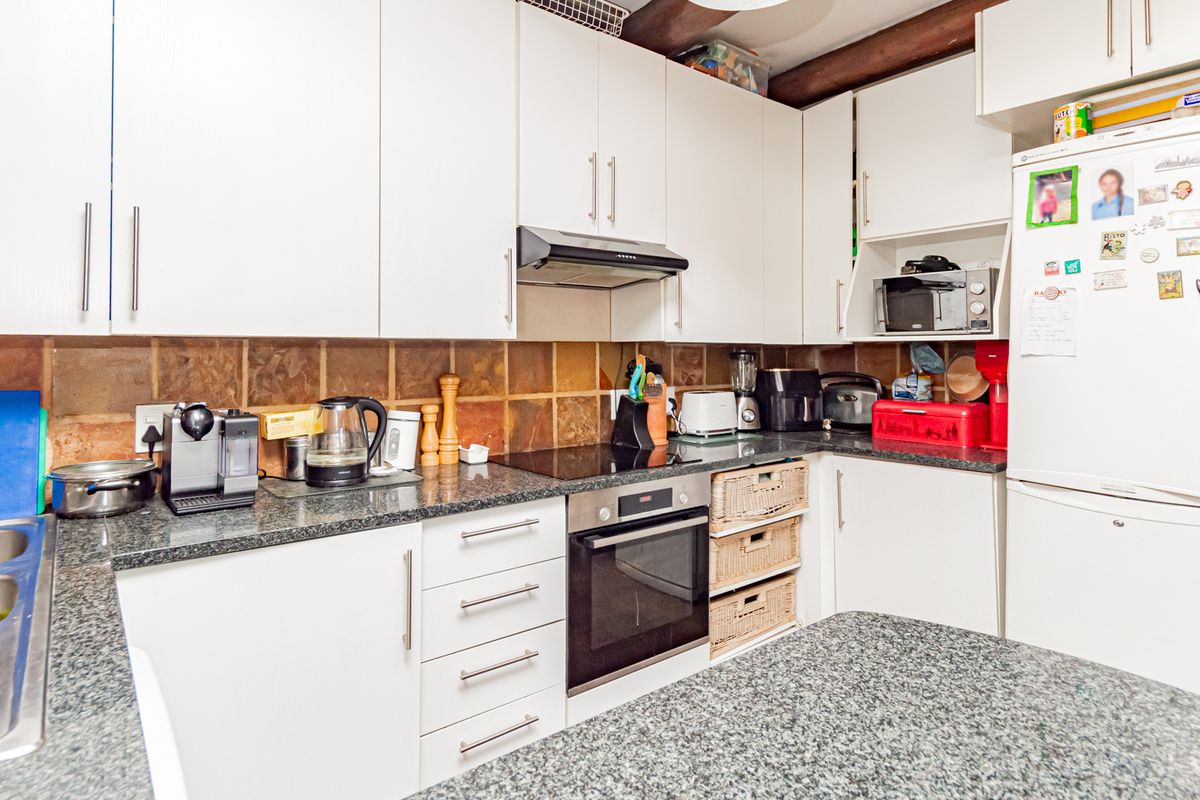 A functional kitchen featuring white cabinetry, granite countertops, a tiled backsplash, and exposed timber ceiling beams, equipped with a built-in oven and hob.