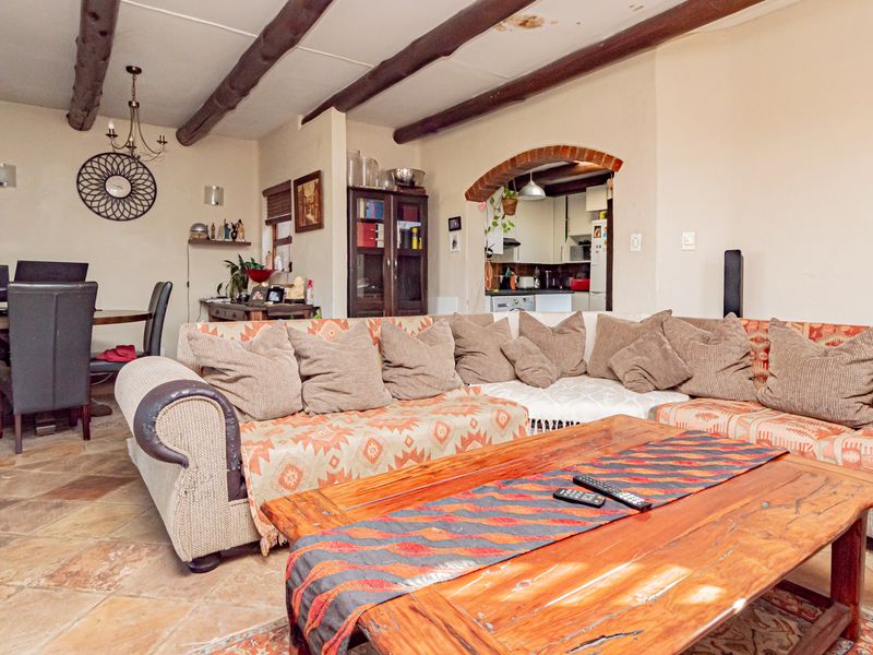 Open plan living and dining area featuring exposed timber ceiling beams, terracotta floor tiles, and a brick archway leading to the kitchen.