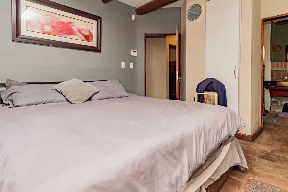Spacious bedroom featuring exposed timber ceiling beams, tiled flooring, and an en-suite bathroom access with built-in cupboard storage.