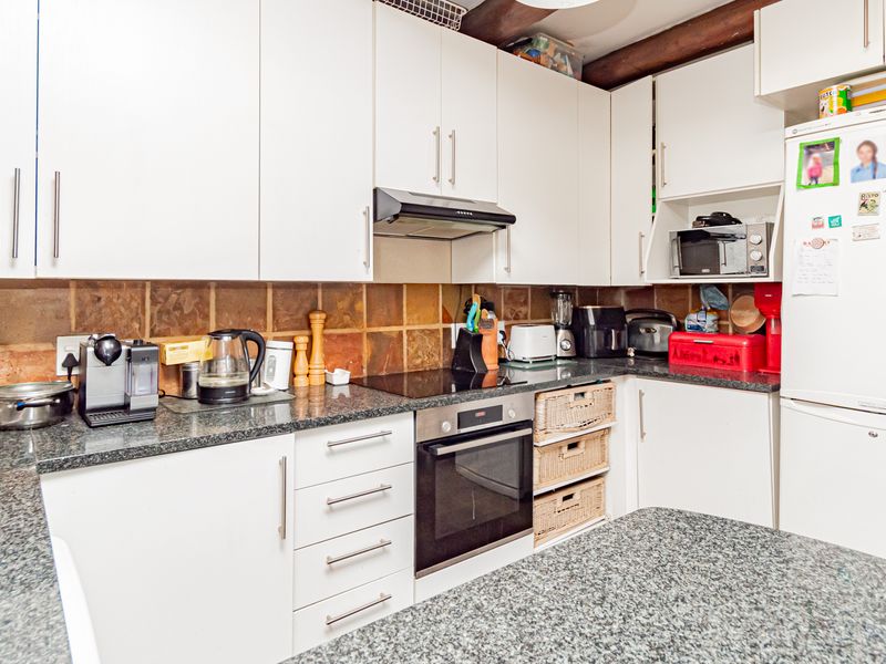 A functional kitchen featuring white cabinetry, granite countertops, a tiled backsplash, and exposed timber ceiling beams, equipped with a built-in oven and hob.