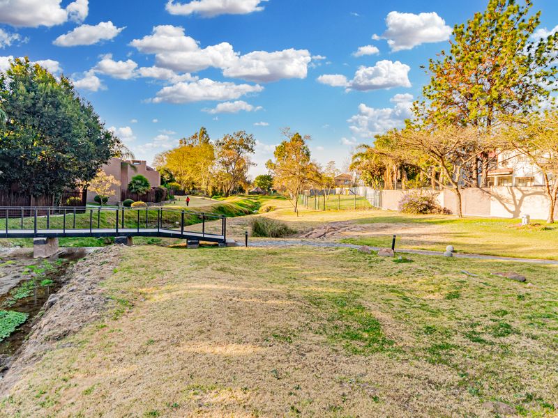 A well-maintained communal garden area featuring a pedestrian bridge over a small water feature and expansive lawn space within the townhouse complex.