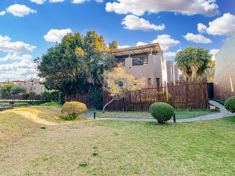 Rear view of the townhouse featuring a private garden, paved walkway, timber fencing, and an elevated covered balcony.