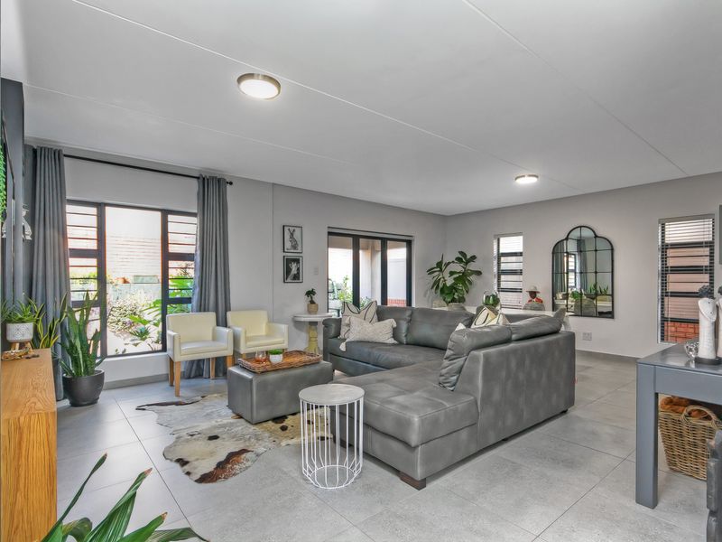 Spacious open-plan living area featuring large format floor tiles, modern aluminium window frames, and sliding doors providing access to the outdoor space.